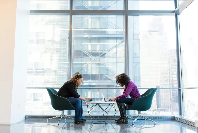 Two individuals sitting on two chairs looking toward each other talking
